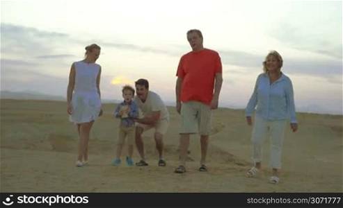 Slow motion steadicam shot of a family evening walk on the beach. Happy parents grandparents and child sitting on dads shoulders