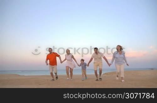 Slow motion steadicam shot of a family of five holding hands and running on the beach. Happy vacation with fun