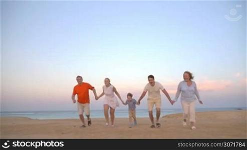 Slow motion steadicam shot of a family of five holding hands and running on the beach. Happy vacation with fun