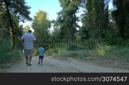 Slow motion steadicam shot of a grandfather and little grandson running down the road in the woods, back view