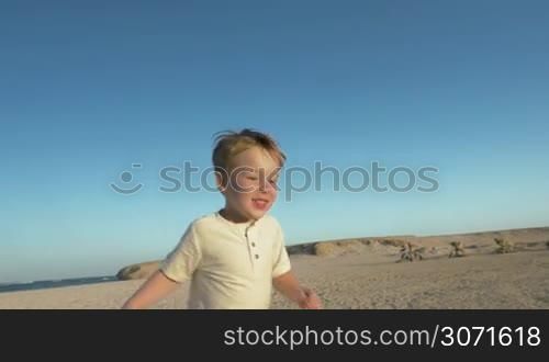Slow motion steadicam shot of a happy little boy running on the beach and meeting his dear father who taking him up
