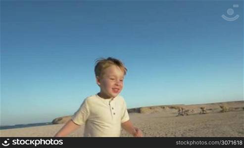 Slow motion steadicam shot of a happy little boy running on the beach and meeting his dear father who taking him up