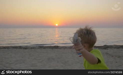 Slow motion steadicam shot of a little boy with toy plane running along the beach to parents. Mother taking him in arms and embracing. Happy parenthood