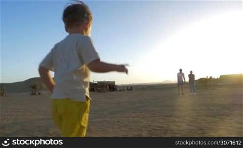 Slow motion steadicam shot of a little child running to the parents on the beach. Then father holding him in arms, hugging and mother kissing dear child. Family renunion