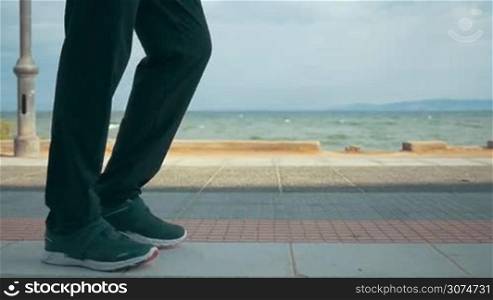 Slow motion steadicam shot of a man running along the sea front with only legs and feet to be seen. Healthy lifestyle with regular sport trainings