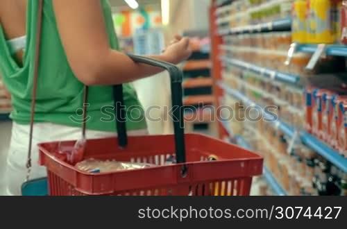 Slow motion steadicam shot of a woman with plastic shopping cart walking along the shelves in the supermarket. Shopping for food
