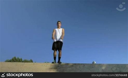 Slow motion steadicam shot of a young athlete performing somersault in a jump from the wall on blue sky background. Extreme hobby