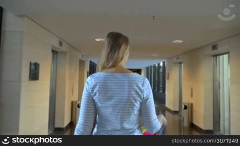 Slow motion steadicam shot of a young happy woman turning to the camera and throwing colorful bags on the shoulder while walking in the hotel hall. Shopping time