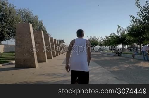 Slow motion steadicam shot of a young sportsman showing parkour skills. He sliding on stone bench and doing somersault