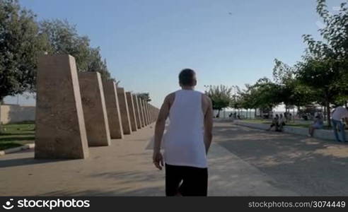 Slow motion steadicam shot of a young sportsman showing parkour skills. He sliding on stone bench and doing somersault