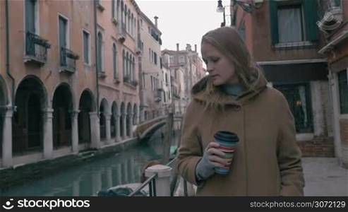 Slow motion steadicam shot of a young woman in coat wandering in the street of Venice. She having coffee during the walk