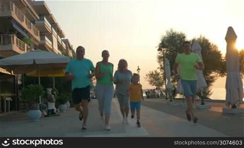 Slow motion steadicam shot of big happy family finishing jog along the seafront at sunset. Parents, child and grandparents giving high-fives to each other