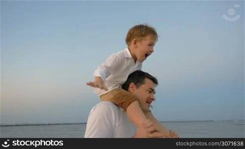 Slow motion steadicam shot of father and son playing in plane takeoff on the beach. Boy sitting on dads shoulders