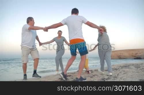 Slow motion steadicam shot of friendly and united family dancing in a circle on the beach. Vacation at the seaside