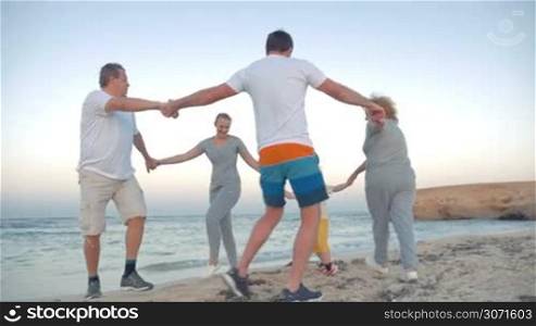 Slow motion steadicam shot of friendly and united family dancing in a circle on the beach. Vacation at the seaside