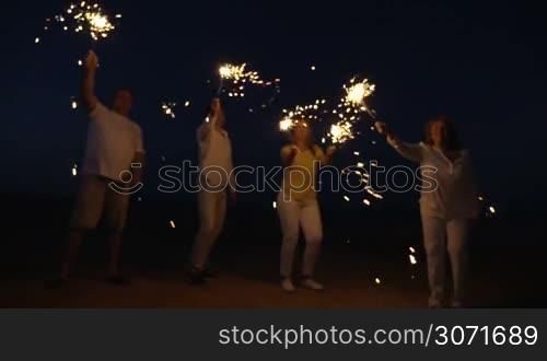 Slow motion steadicam shot of friends or family with firework sparklers on the beach at night. Celebration time