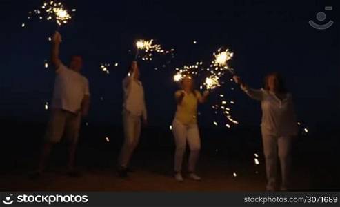 Slow motion steadicam shot of friends or family with firework sparklers on the beach at night. Celebration time