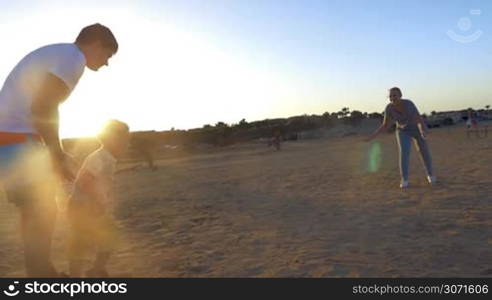 Slow motion steadicam shot of little son running from father to mother and she spinning him around agianst bright sunshine