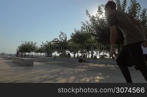 Slow motion steadicam shot of parkour man doing tricks in the city. He running and sliding on stone benches and making somersault in bright sunlight