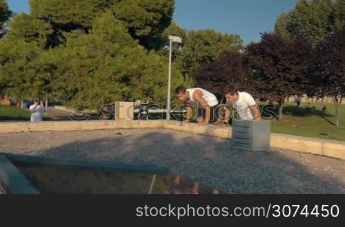 Slow motion steadicam shot of two men doing parkour in the city park. Young people having risky and extreme sportive hobby