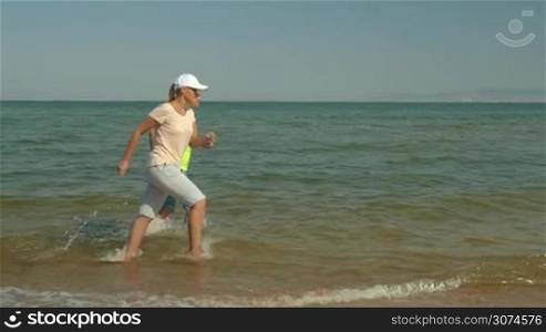 Slow motion steadicam shot of young happy man and woman running in sea and splashing water. Refreshing jogging on hot summer day