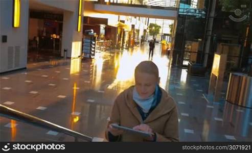 Slow motion steadicam shot of young smiling woman using tablet computer while walking upstairs in modern sunlit trade or business centre