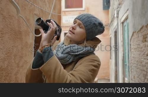 Slow motion steadicam shot of young woman tourist shooting video of old architecture with retro camera