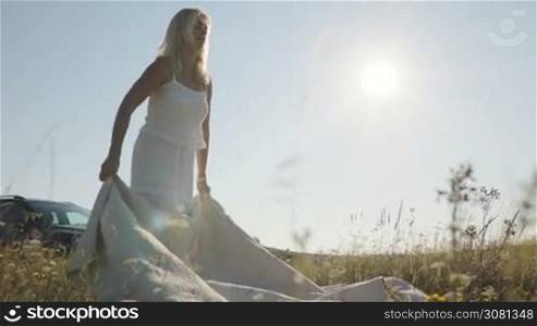 Slow motion. Woman putting a blanket on the ground on nature at sunset