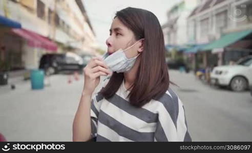 SLOW motion, young Asian woman wear mask on the street side, standing at center, covid-19 corona, virus spreading prevention, healthcare concept, Day time, new normal life 2020, protective medical