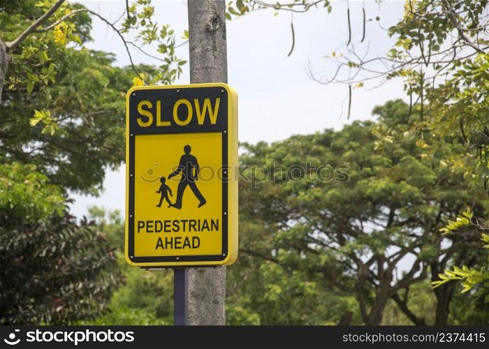 ""Slow pedestrian ahead" traffic sign with black letters and symbols on a yellow background."