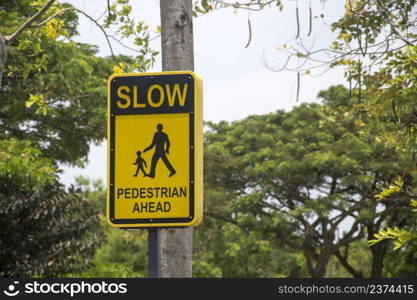 ""Slow pedestrian ahead" traffic sign with black letters and symbols on a yellow background."