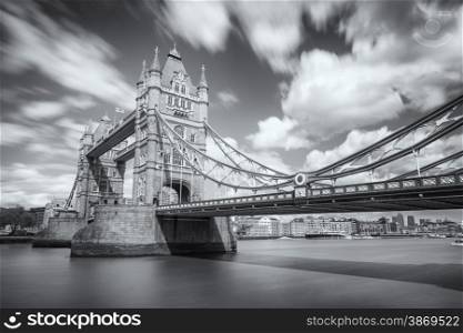Slow shutter black &amp; white image of Tower Bridge over a blurred river Thames in London with flags flying, clear skies and fluffy clouds