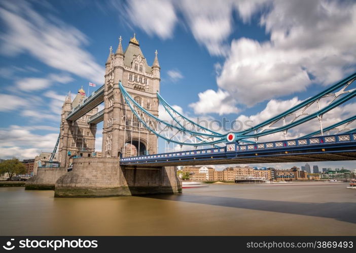 Slow shutter image of Tower Bridge over a blurred river Thames in London with flags flying, blue skies and fluffy clouds