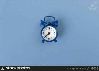 Small alarm clock on pastel background in Classic Blue colour, close-up, top view. Minimal retro style. Time management, Color of the year 2020 concept. Copy space for text. Horizontal orientation.