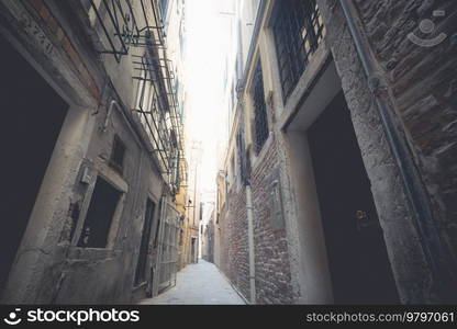 Small alley passage in Venice Italy with tall grunge buildings and bars in the windows