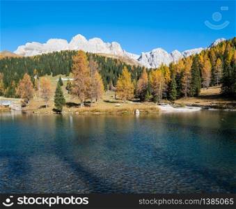 Small autumn alpine mountain pond not far from San Pellegrino Pass, Trentino, Dolomites Alps, Italy. Cima Uomo rocky massif in far. Picturesque traveling, seasonal and nature beauty concept scene.