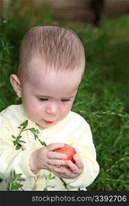 small baby holding apple in green grass