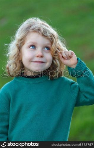 Small blond child with green jersey imagining something in the field