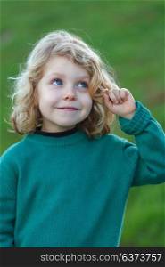 Small blond child with green jersey imagining something in the field