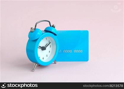 Small blue alarm clock is next to blue credit card. The concept of modern fast online banking and instant financial operations. Small blue alarm clock and blue credit card