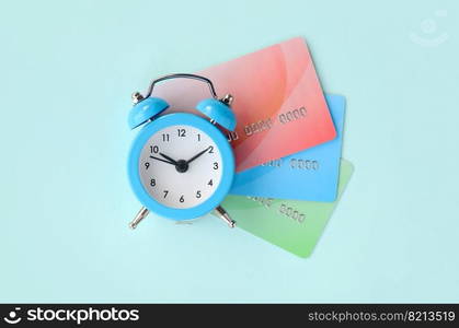 Small blue alarm clock lies on colored credit cards. The concept of modern fast online banking and fast financial operations. Modern fast online banking and funds transfer operations