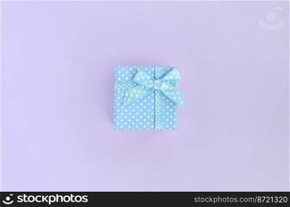 Small blue gift box with ribbon lies on a violet background. Minimalism flat lay top view.. Small blue gift box with ribbon lies on a violet background. Minimalism flat lay top view