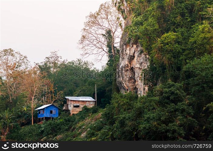 Small blue local cottages in forest and rock cliff in Asian tropical forest - Luang Prabang, Laos