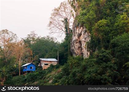 Small blue local cottages in forest and rock cliff in Asian tropical forest - Luang Prabang, Laos