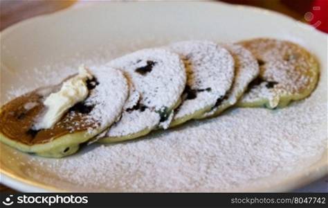 Small blueberry pancakes topped with melting butter and powered sugar in horizontal image with copy space.