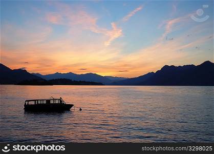 Small boat anchored in quite lake water before the dawn; Maggiore Lake, Italy.