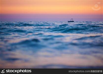 Small boat on waves at sunset, focus on the boat, blurred foreground, copy space