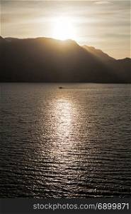 Small boat sailing in the sea at sunset with mountains on background. Small boat sailing in the sea