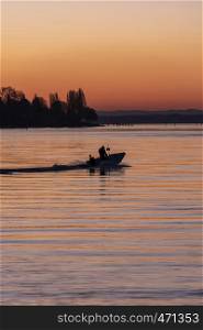 Small boat silhouette driving on the lake Bodensee from south Germany. Beauitful summer sky at sunrise