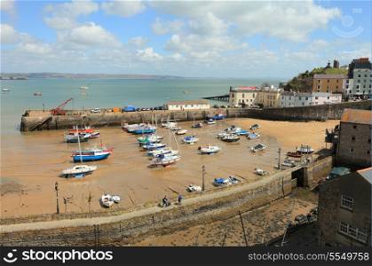 Small boats lie stranded on the sand in Tenby Harbour, West Wales, UK, at low tide.